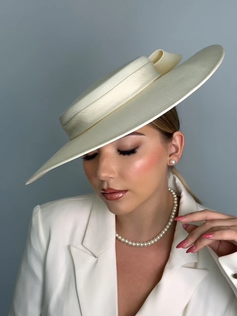 Soft glam with a rosy flush and glossy lip under an ivory wide-brim hat, eyes down