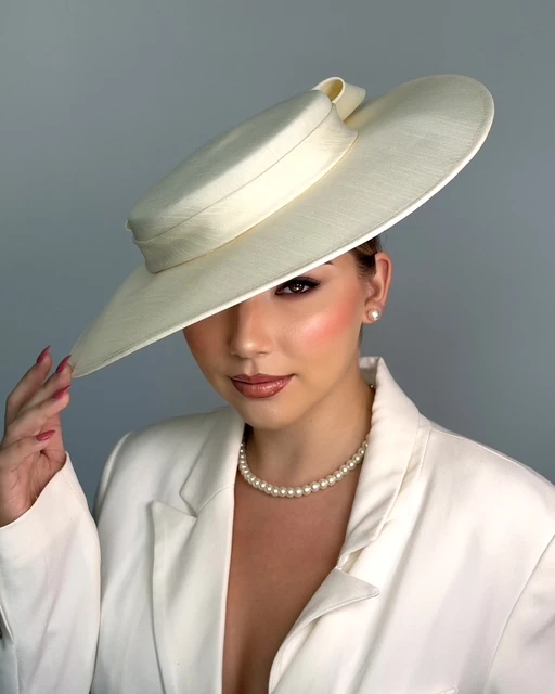 Soft glam makeup under a wide-brim ivory hat, hand on the brim, with pearls